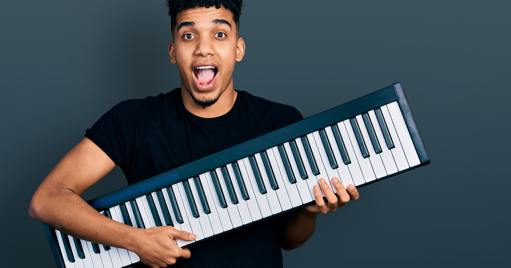 A young man with an excited expression holds a sleek digital piano keyboard