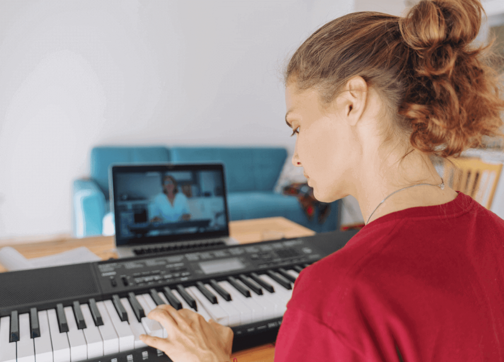 A woman playing a digital piano keyboard while a tablet displays a piano tutorial video