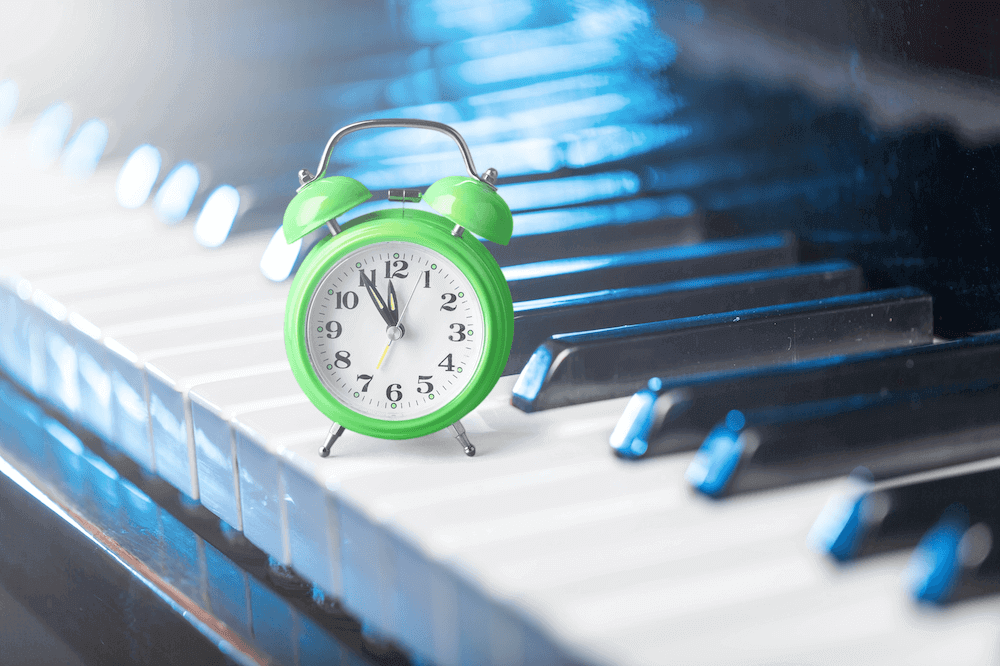 A green alarm clock sitting atop the white keys of a piano