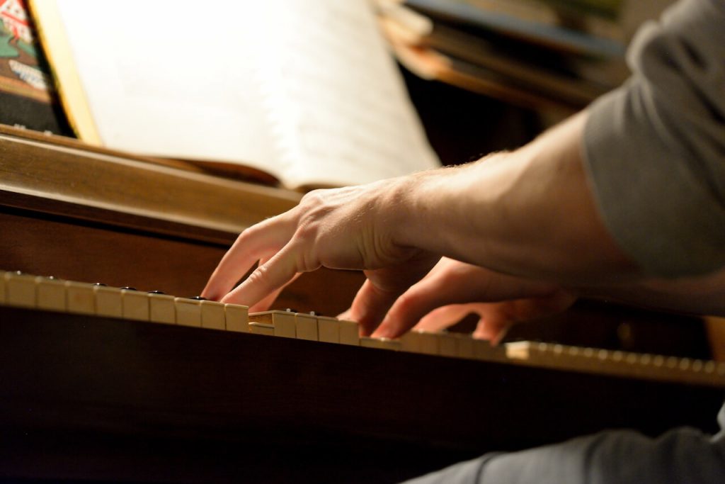 Two hands playing an acoustic piano with sheet music on the music rest